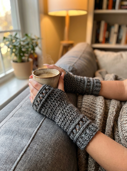 Fern Gully Crochet Fingerless Gloves Pattern - seated on a sofa holding a warm mug
