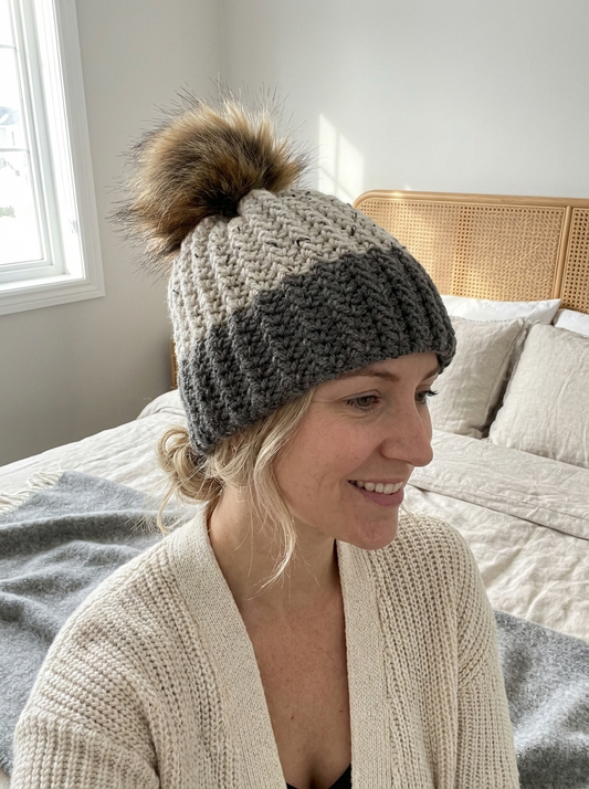 Woman wearing the Plume Grass crochet beanie in charcoal and cream tweed with faux fur pompom