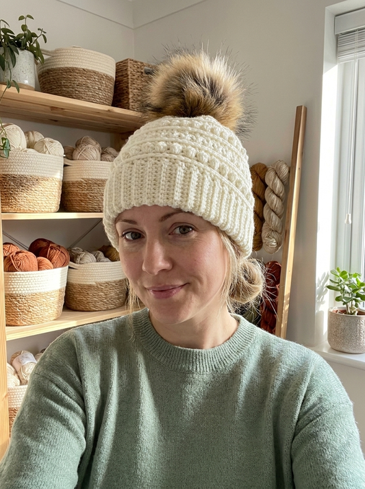 Woman wearing the Quince Blossom crochet beanie in cream with bobble bands and faux fur pompom